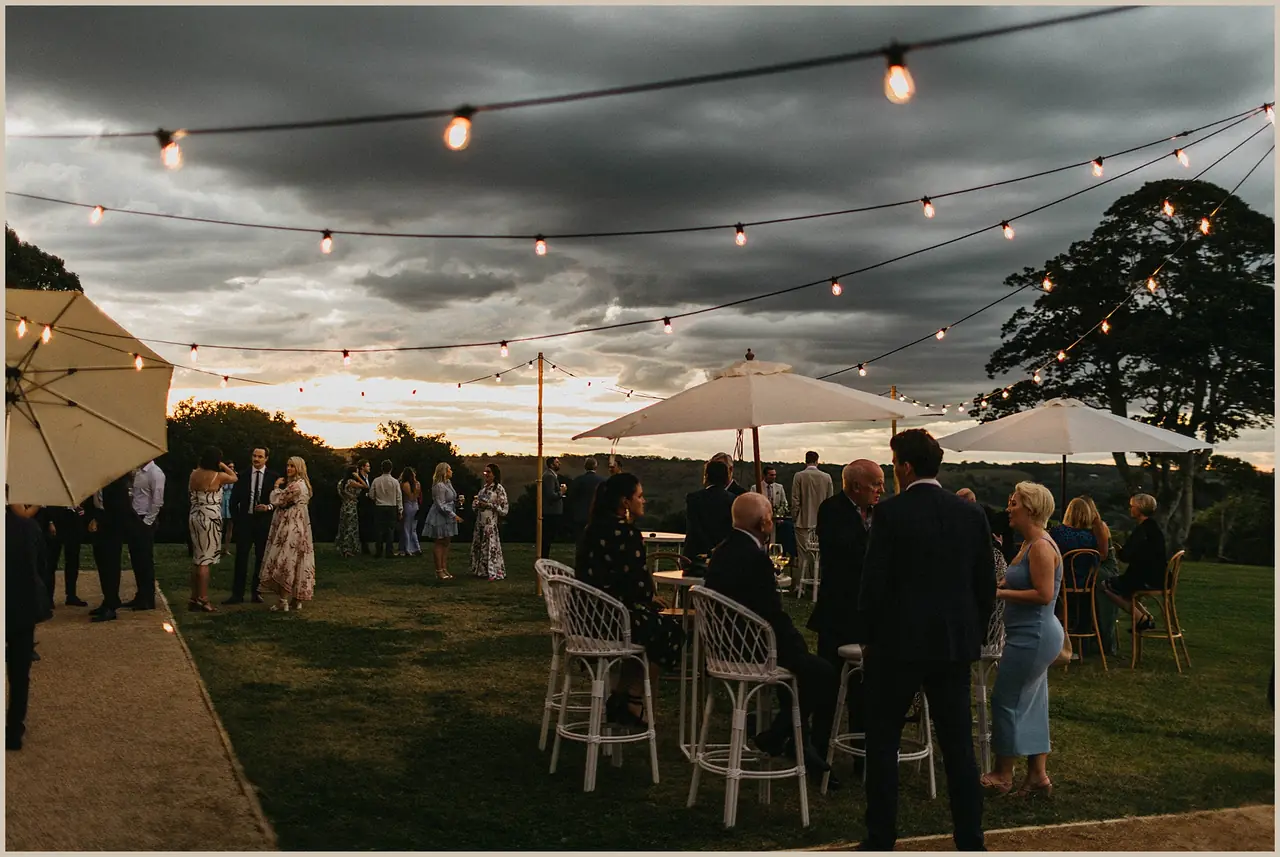 Jess & Rich at The Orchard Estate: Guests mingle outside beneath festoon lights at dusk.