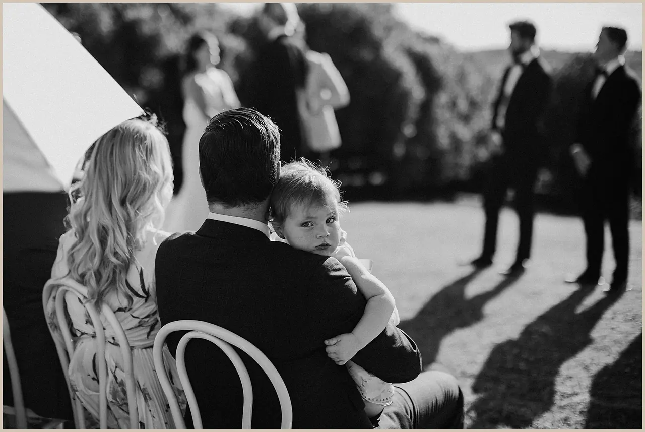 Jess & Rich at The Orchard Estate: A guest holds a small child during the outdoor ceremony.