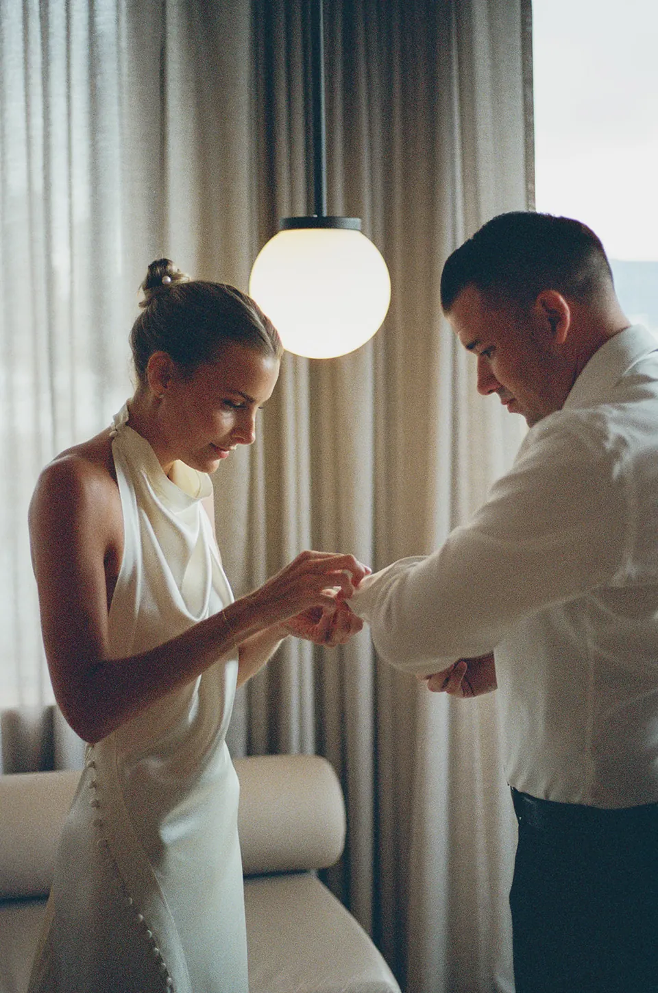 Clare and Matt helping each other get ready beside a window in their Calile suite.