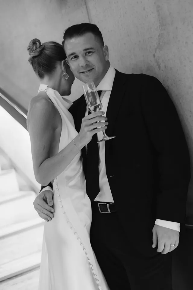 Black-and-white portrait of Clare leaning into Matt with a champagne flute.